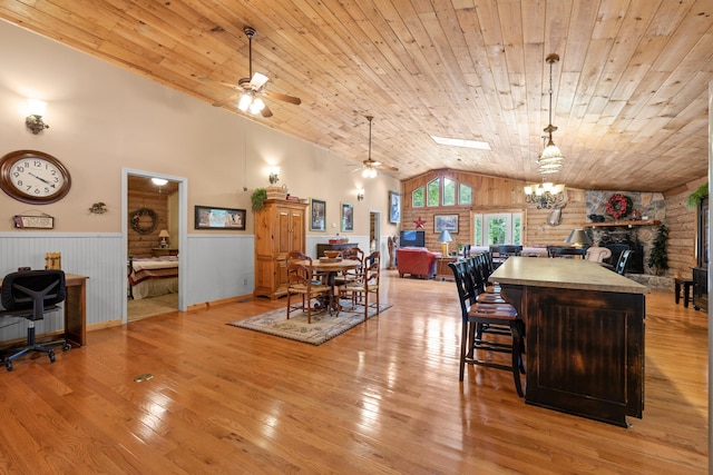 dining area featuring wood ceiling, wainscoting, light wood-style flooring, and a stone fireplace