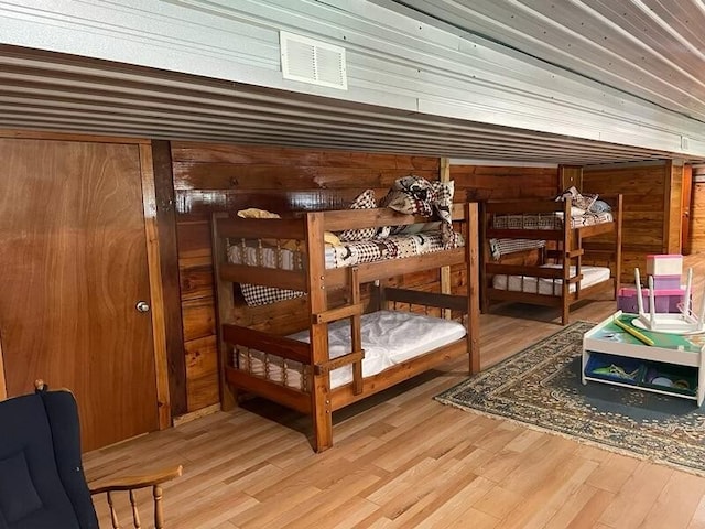 bedroom featuring wood finished floors, visible vents, and wooden walls