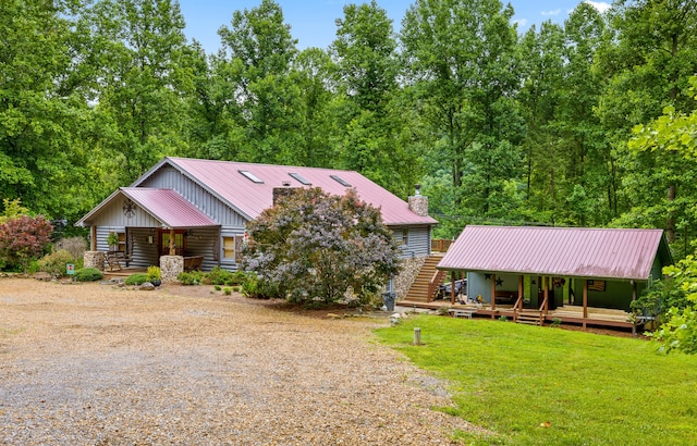 view of front of property featuring metal roof, covered porch, driveway, a front lawn, and a chimney