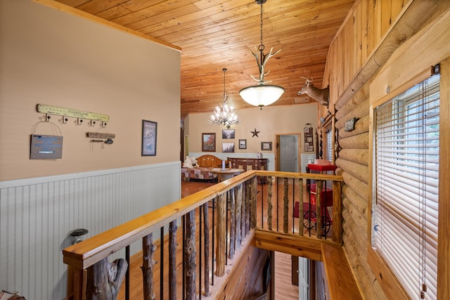 corridor featuring rustic walls, wainscoting, wood ceiling, an upstairs landing, and a notable chandelier