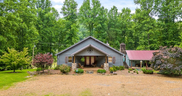 view of front facade featuring metal roof, a porch, log siding, a chimney, and a front yard