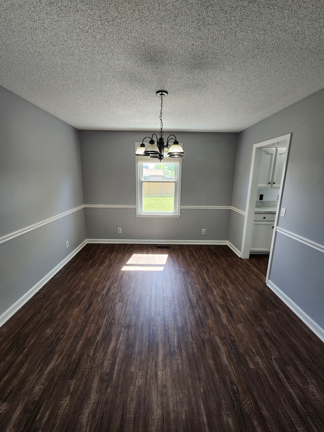 spare room with dark hardwood / wood-style flooring, an inviting chandelier, and a textured ceiling