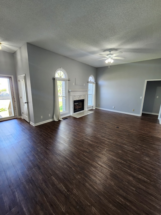 unfurnished living room featuring a high end fireplace, dark hardwood / wood-style flooring, ceiling fan, and a wealth of natural light