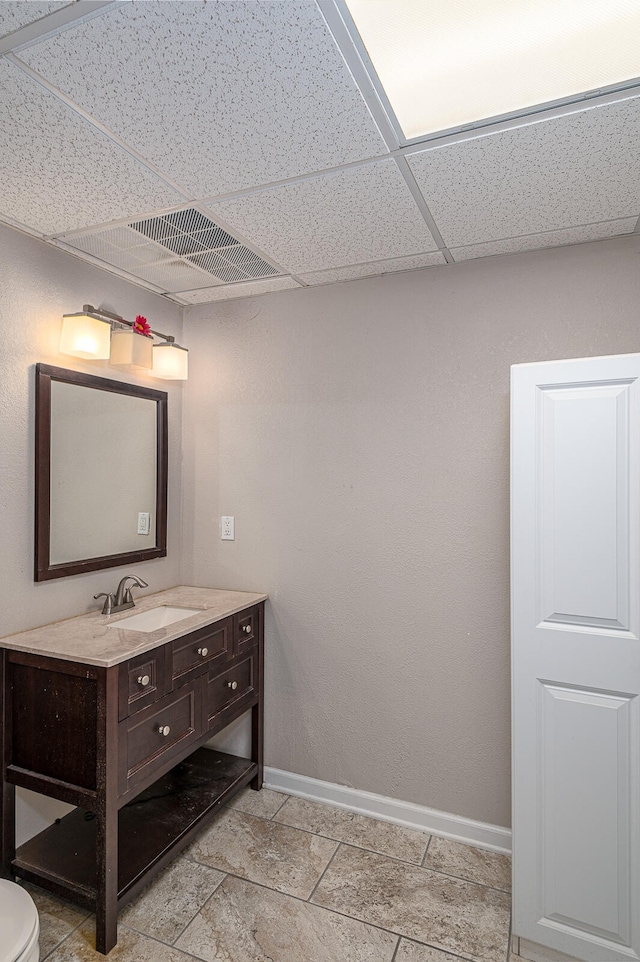 bathroom with toilet, vanity, a drop ceiling, and tile flooring