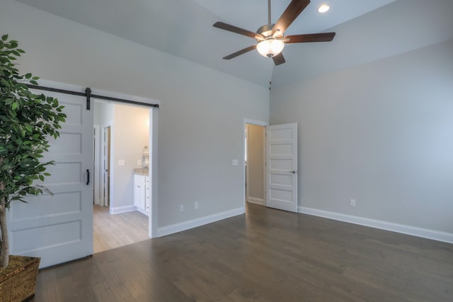 unfurnished bedroom featuring high vaulted ceiling, a barn door, ceiling fan, ensuite bathroom, and dark hardwood / wood-style floors