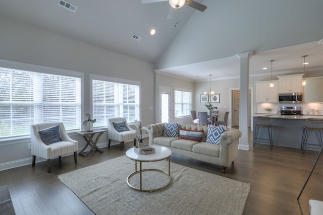 living room featuring dark hardwood / wood-style flooring, high vaulted ceiling, ceiling fan with notable chandelier, and ornate columns