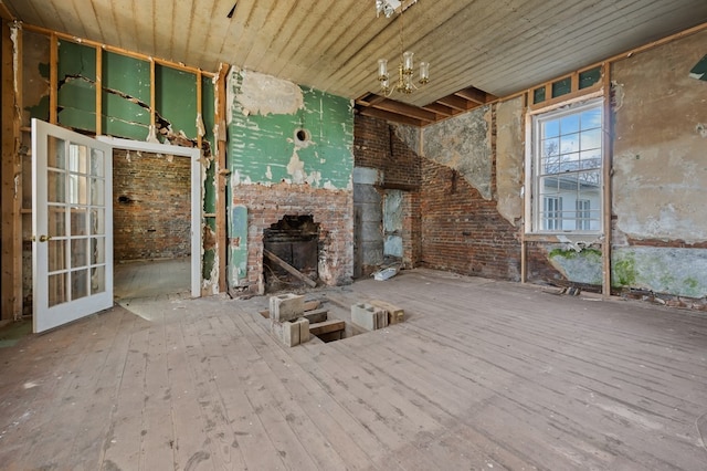 unfurnished living room featuring wooden ceiling, an inviting chandelier, hardwood / wood-style flooring, brick wall, and a fireplace