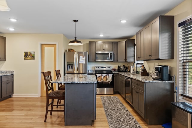 kitchen with decorative light fixtures, light hardwood / wood-style floors, stainless steel appliances, and light stone countertops