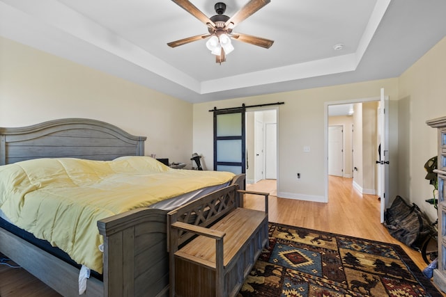 bedroom featuring light hardwood / wood-style flooring, ceiling fan, a barn door, and a tray ceiling