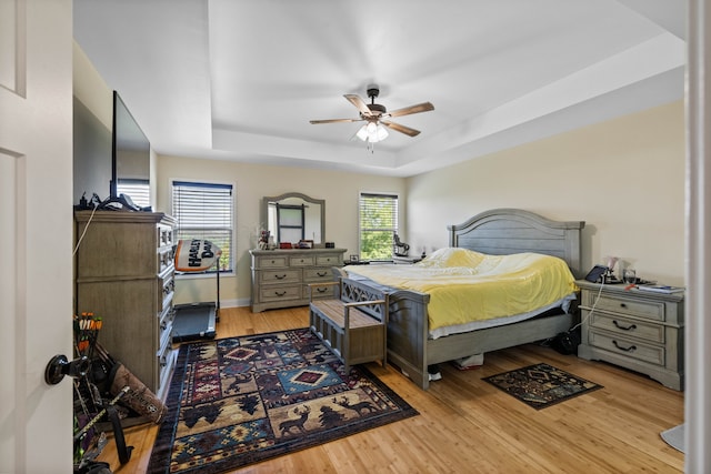 bedroom featuring light hardwood / wood-style flooring, ceiling fan, and a tray ceiling