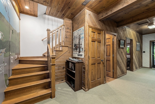 stairway featuring wooden walls, wooden ceiling, and light colored carpet