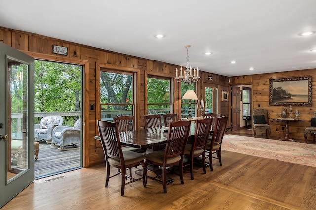 dining area with plenty of natural light, an inviting chandelier, wood walls, and light hardwood / wood-style flooring