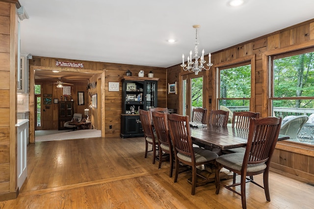 dining area featuring wood walls, light hardwood / wood-style flooring, and ceiling fan with notable chandelier