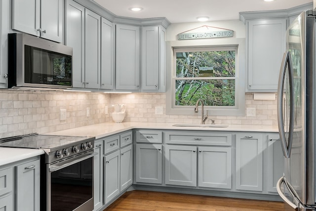 kitchen with backsplash, stainless steel appliances, sink, and light hardwood / wood-style flooring