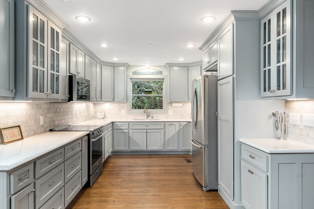 kitchen featuring hardwood / wood-style floors, gray cabinetry, backsplash, appliances with stainless steel finishes, and sink