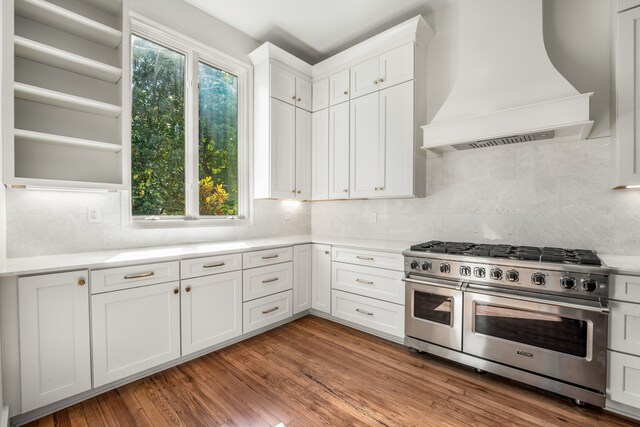 kitchen featuring wood-type flooring, premium range hood, tasteful backsplash, white cabinetry, and range with two ovens