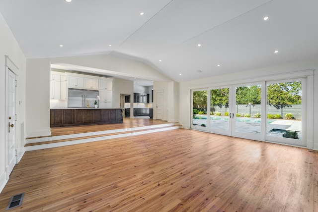 unfurnished living room with lofted ceiling, french doors, and light wood-type flooring