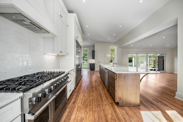 kitchen with high quality appliances, a kitchen island, light stone countertops, light hardwood / wood-style flooring, and white cabinetry