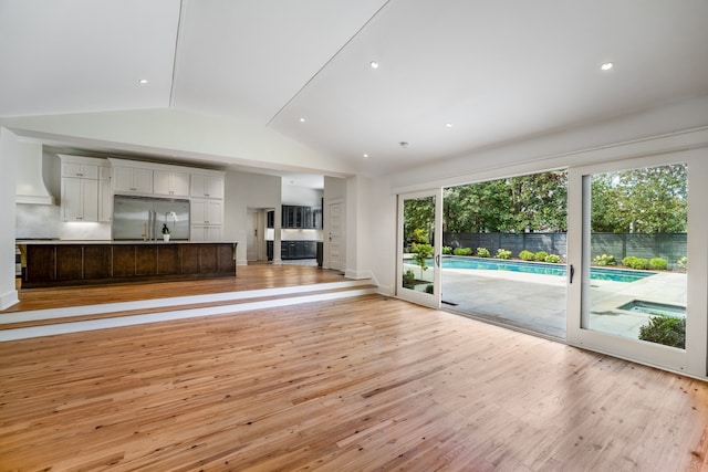 unfurnished living room featuring lofted ceiling, a healthy amount of sunlight, and light wood-type flooring