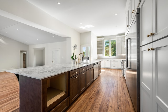 kitchen with white cabinets, a center island with sink, light hardwood / wood-style flooring, and light stone counters