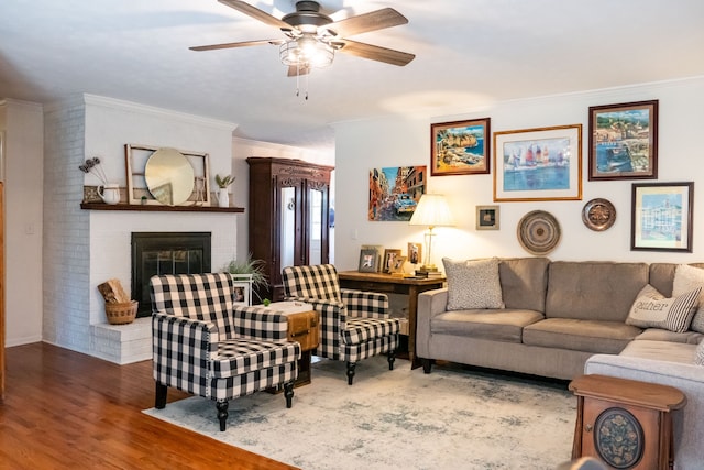 living room with ceiling fan, brick wall, a brick fireplace, hardwood / wood-style flooring, and ornamental molding