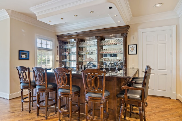 bar featuring light hardwood / wood-style flooring, ornamental molding, and dark stone countertops