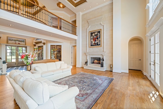 living room with crown molding, light wood-type flooring, a towering ceiling, and french doors