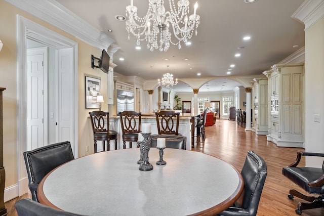 dining space featuring light wood-type flooring, ornamental molding, a chandelier, and decorative columns