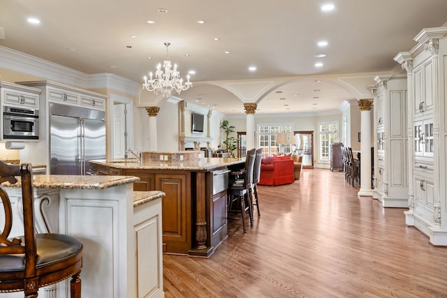 kitchen with appliances with stainless steel finishes, a chandelier, ornate columns, a breakfast bar area, and an island with sink