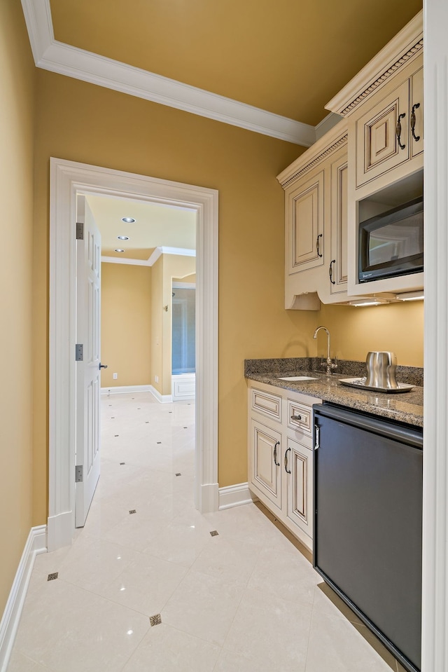 kitchen with ornamental molding, black microwave, light tile floors, and cream cabinets