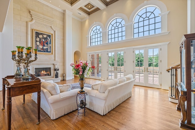 living room featuring light wood-type flooring, coffered ceiling, crown molding, a high ceiling, and french doors