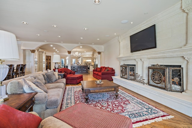 living room with crown molding, light hardwood / wood-style floors, a fireplace, and ornate columns