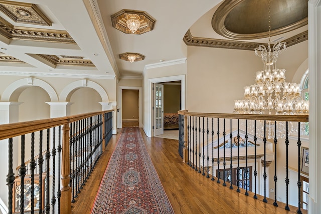 corridor featuring coffered ceiling, a notable chandelier, crown molding, a raised ceiling, and dark hardwood / wood-style flooring