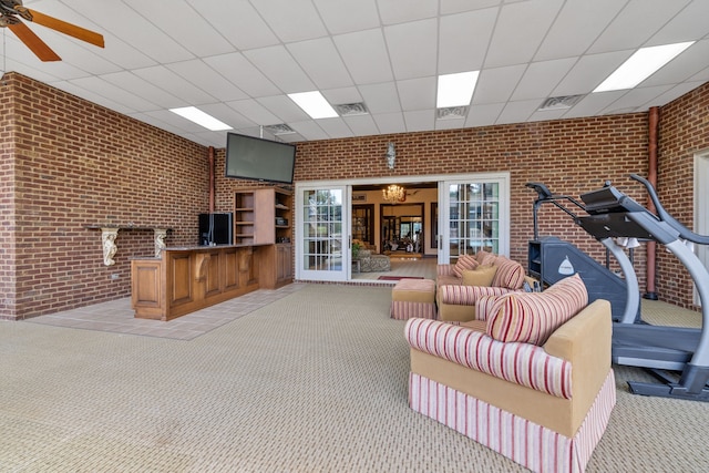 carpeted living room with brick wall, ceiling fan with notable chandelier, and a drop ceiling