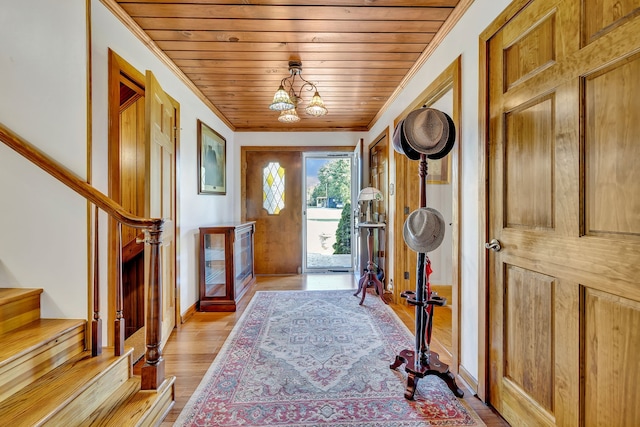 foyer entrance with an inviting chandelier, light wood-type flooring, ornamental molding, and wood ceiling