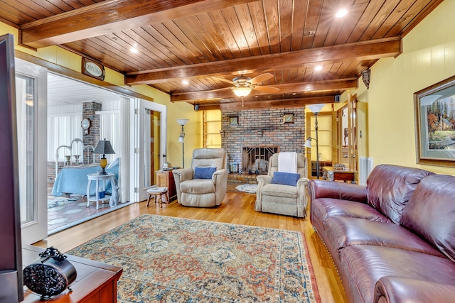 living room featuring wood ceiling, light hardwood / wood-style flooring, a fireplace, ceiling fan, and beam ceiling