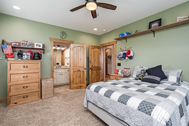 bedroom with ensuite bathroom, light colored carpet, and ceiling fan