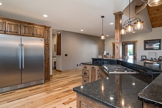 kitchen featuring decorative columns, light hardwood / wood-style flooring, dark stone countertops, stainless steel appliances, and decorative light fixtures