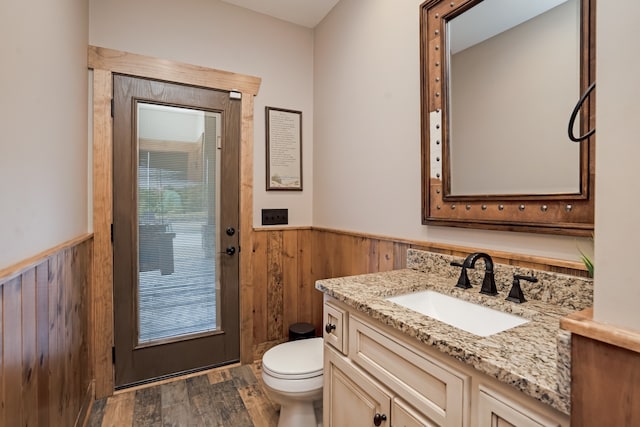 bathroom featuring toilet, wood walls, hardwood / wood-style flooring, and vanity