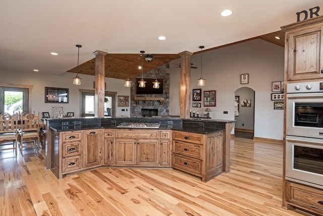 kitchen featuring a fireplace, double oven, hanging light fixtures, light hardwood / wood-style floors, and vaulted ceiling