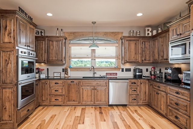 kitchen featuring appliances with stainless steel finishes, sink, light wood-type flooring, and hanging light fixtures