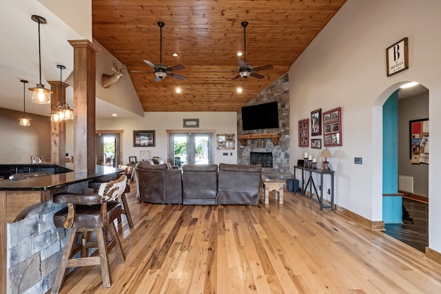 living room with wood ceiling, ceiling fan, high vaulted ceiling, light wood-type flooring, and a stone fireplace