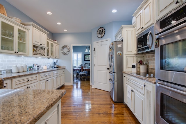 kitchen with light stone countertops, white cabinetry, backsplash, dark wood-type flooring, and stainless steel appliances