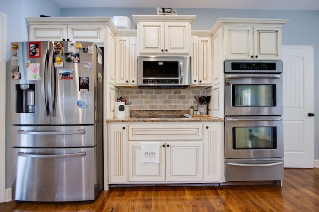 kitchen with light stone countertops, cream cabinetry, appliances with stainless steel finishes, backsplash, and dark hardwood / wood-style floors