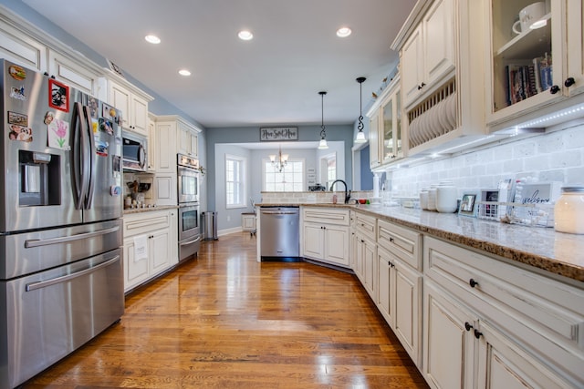 kitchen with hanging light fixtures, appliances with stainless steel finishes, a chandelier, light stone countertops, and dark wood-type flooring