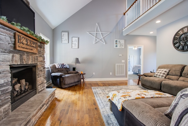 living room featuring light hardwood / wood-style flooring, a stone fireplace, and high vaulted ceiling