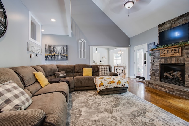 living room featuring high vaulted ceiling, a stone fireplace, hardwood / wood-style flooring, and ceiling fan with notable chandelier