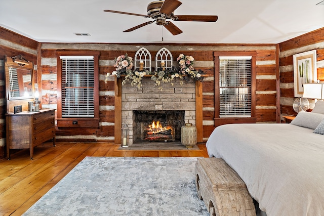 bedroom with wood walls, a stone fireplace, dark hardwood / wood-style floors, and ceiling fan