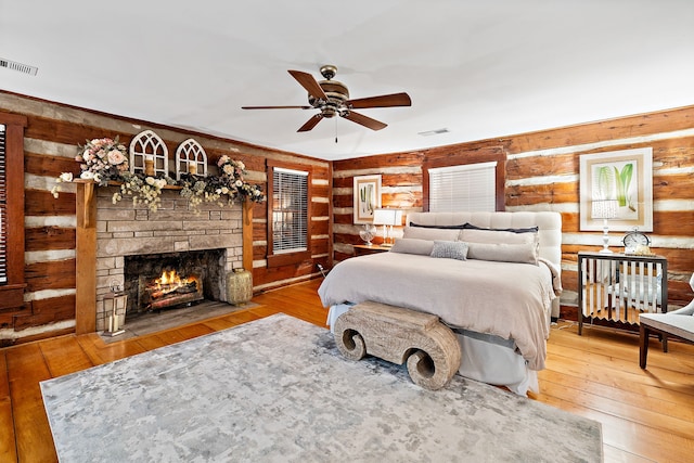 bedroom with rustic walls, ceiling fan, light wood-type flooring, and a fireplace