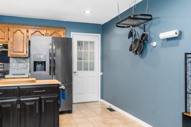 kitchen featuring light tile flooring, backsplash, range hood, and stainless steel fridge with ice dispenser